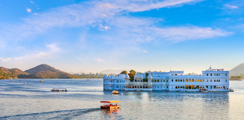 Taj Lake Palace in Udaipur situated in the middle of Lake Pichola with boats and mountains in the background