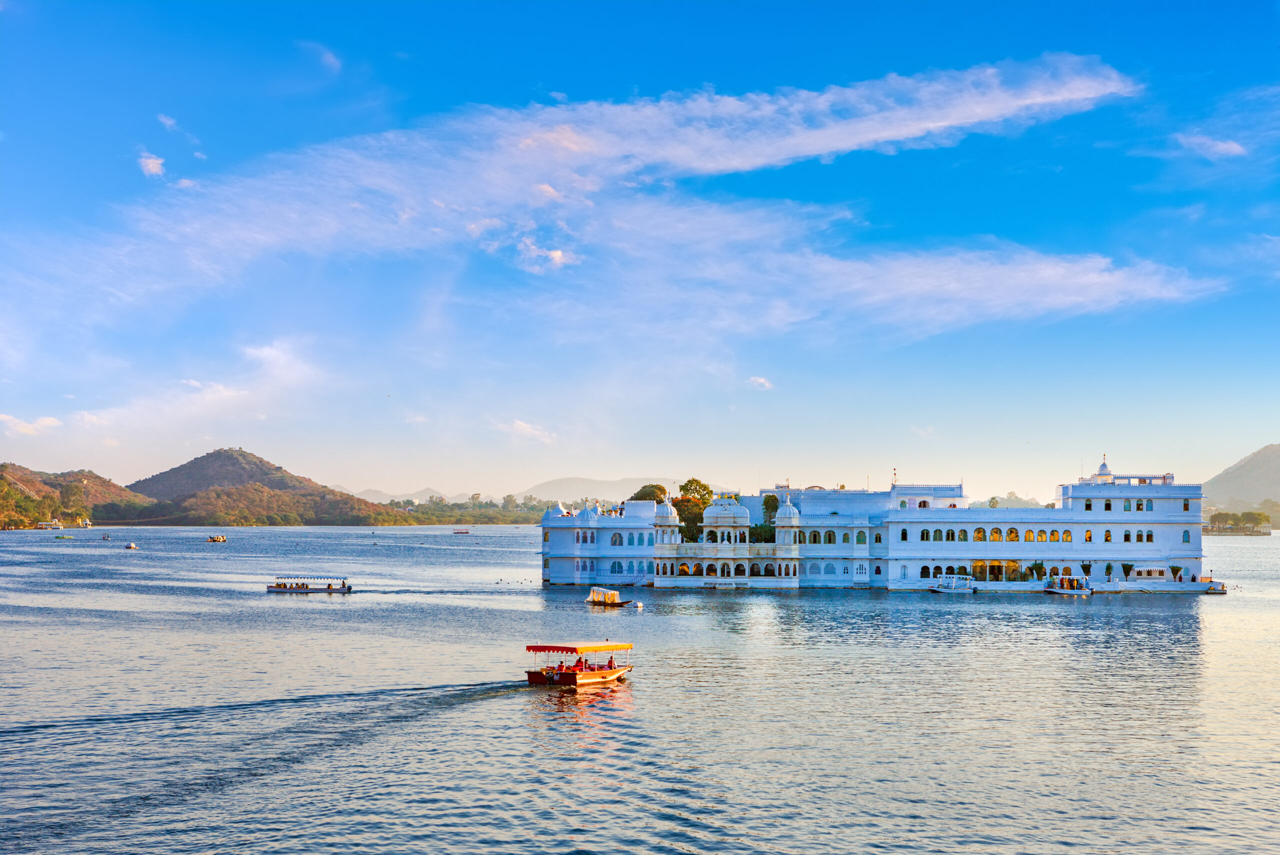 Taj Lake Palace in Udaipur situated in the middle of Lake Pichola with boats and mountains in the background